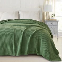 a bed covered in a green bedspread next to a night stand with two lamps