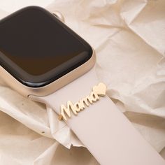 an apple watch sitting on top of a white paper covered surface with the word mama spelled in gold