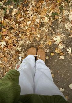 a person standing in front of leaves on the ground with their legs crossed and feet up