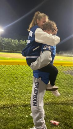 two girls hugging each other on a baseball field at night with lights in the background