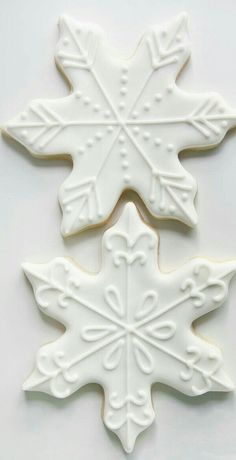 two cookies decorated with white frosting are sitting on a counter top, one is shaped like a snowflake and the other looks like a leaf