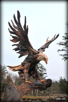 an eagle sculpture sitting on top of a tree stump in the woods with its wings spread