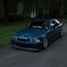 a blue car parked on the side of a road next to some grass and trees