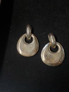 two silver earrings sitting on top of a black surface