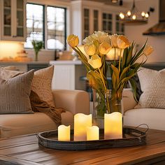 flowers and candles on a tray in front of a living room table with couches