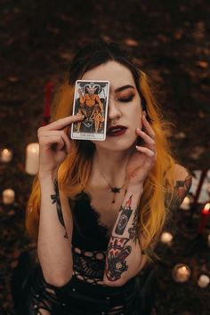 a woman holding up a tarot card in front of her face with candles around her