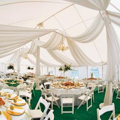 a large tent with tables and chairs covered in white draping, green carpet