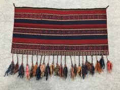 a wall hanging with tassels and beads on the end, in red, brown, black and blue colors