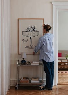 a woman standing in front of a painting on a wall next to a table with a lamp