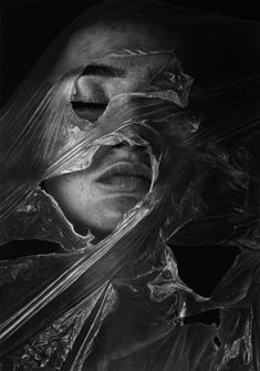 a black and white photo of a woman wrapped in plastic wraps with her eyes closed