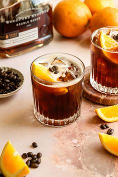 two glasses filled with iced tea and orange slices on a table next to coffee beans