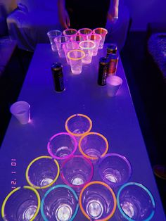 a table topped with lots of glasses and cups on top of each other in front of a purple light