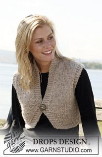 a woman sitting on top of a wooden bench next to the ocean wearing a knitted vest