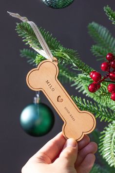 a hand holding a wooden dog bone ornament next to a christmas tree with ornaments