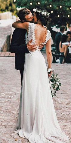 a bride and groom embracing each other in front of an outdoor wedding venue with string lights