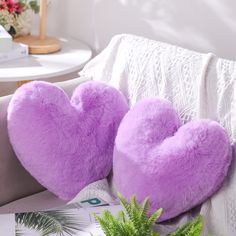 two purple heart shaped pillows sitting on top of a couch next to a potted plant