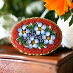 Discover our enchanting vintage Italian mosaic oval brooch from the 1960s. This brooch is a testament to the rich heritage of Italian mosaic jewelry. 🌼 It features a design of delicate white and blue flowers elegantly framed by a vibrant orange mosaic background. The intricate details of the mosaic bring to life the essence of Italian craftsmanship. 🌞 Encased in an oval gold tone frame, this brooch is a wearable work of art that effortlessly blends vintage charm with vibrant color. 🎨The art of mosaic dates back to the Roman Empire. Micro mosaic jewelry became popular in the 17th - 19th centuries as rich European families were touring Europe especially Italy. Italian craftsmen turned their glass making skills into the production of micro mosaic jewelry for their rich visitors. In Italy, Antique Oval Handmade Brooches, Antique Handmade Oval Brooches, Handmade Victorian Oval Brooches, Vintage Oval Brooches For Wedding, Vintage Oval Wedding Brooches, Vintage Oval Brooches For Collectors, Handmade Vintage Brooch For Anniversary, Handmade Vintage Brooches For Anniversary, Heirloom Oval Brooches As Gift