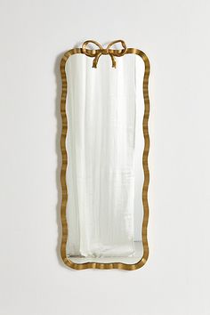 a mirror that is on the wall with a bow around it's edge and gold trim