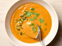 a white bowl filled with carrot soup and topped with green garnish