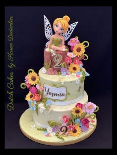 a birthday cake with a tinker fairy sitting on it's side and flowers around the edges