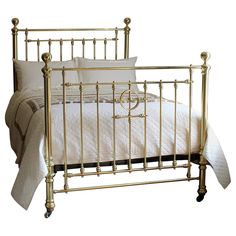 a gold metal bed with white sheets and pillows