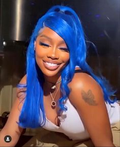 a woman with bright blue hair and tattoos on her chest smiles at the camera while wearing a white tank top