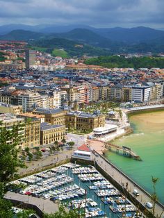 an aerial view of a city with boats docked in the water and mountains in the background