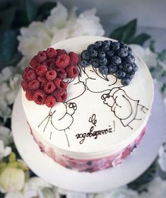 a cake with berries and blueberries on it sitting next to some white flowery branches