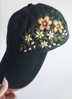 a person holding up a black hat with flowers embroidered on the front and side of it