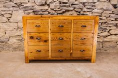 a wooden dresser sitting in front of a stone wall with lots of drawers on it