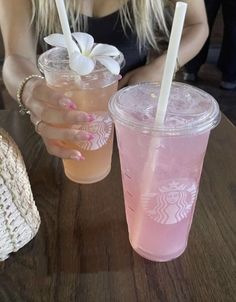 a woman sitting at a table with two drinks in front of her and one holding a straw hat