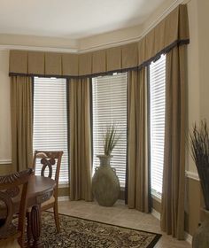 a dining room table and chairs in front of two windows with drapes on them