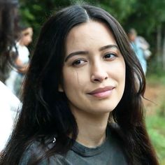 a close up of a person with long hair and wearing a black shirt in front of trees