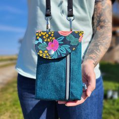 a person holding a small purse with flowers on the front and side, in their hands