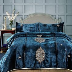 a bed covered in a blue comforter next to a night stand with flowers on it