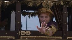 a man dressed in medieval costume waving out the window from inside a train with gold trimmings