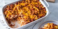 a casserole dish with meat and cheese in it on a table next to two plates