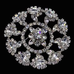 This large round pin is a fine example of the vintage large rhinestone pins with these amazing designs and brilliant that are hard to find. The pin is a three dimensional design with at center large chaton rhinestones domed flower  the shape of flower is surrounded by many medium Marquise rhinestone accentuated by smaller round chaton rhinestones.   the outer row is made up of more large Marquise faceted shaped clear rhinestones surrounded by  medium round rhinestones all in a silvertone setting Crystal Rhinestone Brooches For Costume Jewelry, Crystal Rhinestone Brooches Costume Jewelry, Elegant Round Brooches With Rhinestones, Elegant Round Rhinestone Brooches, Round Brooches With 17 Jewels For Wedding, Anniversary Rhinestone Round Brooches, Anniversary Round Rhinestones Brooches, Anniversary Brooches With Rhinestones, Round Wedding Brooch With 17 Jewels