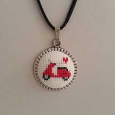 a cross stitch necklace with a red bus on it's front and black cord