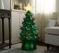 a green christmas tree with lights on it in front of a couch and window sill