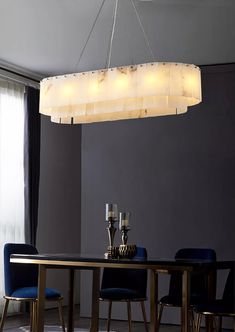 a chandelier hanging over a dining room table with blue chairs and vases