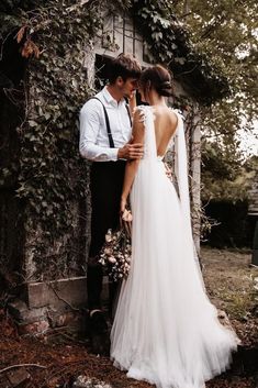 a bride and groom standing next to each other in front of an ivy covered wall