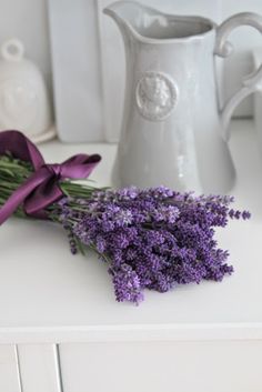 a bunch of purple flowers sitting on top of a white table next to a vase