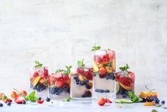 four glasses filled with fruit and ice on top of a white table covered in snow