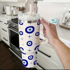 a hand holding a coffee cup in front of a stove top oven with an evil eye design on it