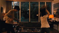 two people dancing in a living room near a window with large panoramic windows