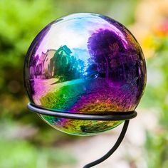 a colorful glass ball sitting on top of a metal stand in front of some bushes