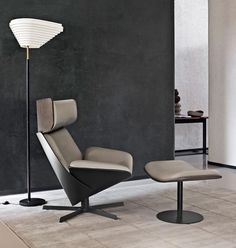 a modern chair and footstool in front of a black wall with a lamp on it