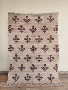 an old rug with purple flowers on it sitting on a wooden floor in front of a white wall