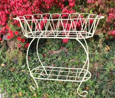 a white wire basket sitting on top of a lush green field next to red flowers